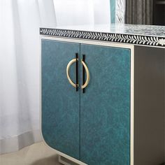 a blue cabinet with gold handles in front of a white curtain and curtains behind it