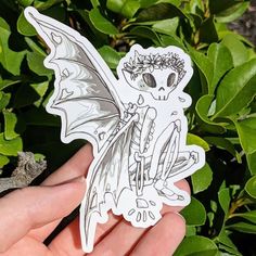 a hand holding a sticker with a skeleton on it and a dragon in the background