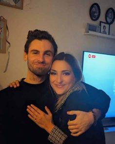 a man and woman hugging each other in front of a tv