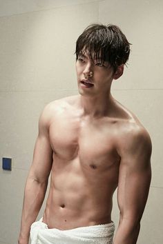 a shirtless young man standing in front of a bathroom mirror wearing a towel around his waist