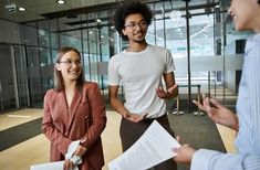 two men and a woman are talking in an office building while one man is holding papers