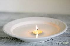 a lit candle in a white bowl on a table