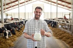 a man standing in a barn holding a jug of milk and smiling at the camera