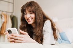 a woman laying on the bed looking at her cell phone and smiling as she lays down