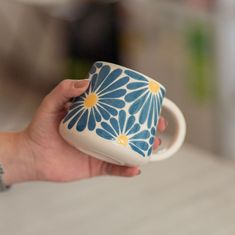 a hand holding a blue and white coffee cup with yellow daisies on the inside