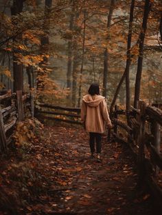 a woman walking down a path in the woods with fall leaves on the ground and trees around her