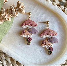 two pink and purple earrings sitting on top of a white plate next to a plant