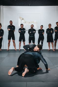 two men wrestling in front of a group of people wearing wetsuits and standing behind them