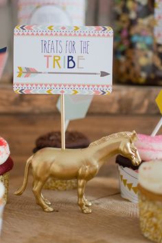 there are cupcakes with gold horses on them and a sign that says treats for the tribe