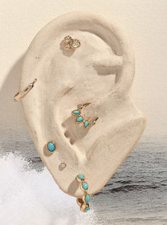 an ear with turquoise stones on it near the ocean and sand in front of water