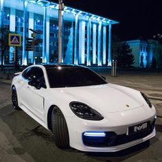 a white sports car is parked in front of a building at night with blue lights