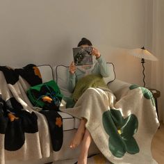 a person sitting on a couch with a blanket over their head, reading a book