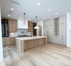 an empty kitchen with wooden floors and white cabinets in the center, surrounded by hanging lights