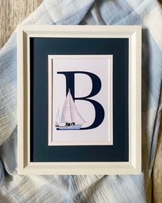 a framed letter b with a sailboat in the water on a blue and white blanket