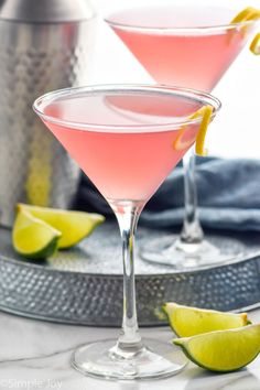 two glasses filled with pink lemonade and garnished with limes on a tray