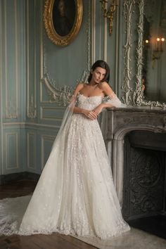 a woman in a wedding dress standing next to a fireplace with her hands on her hips