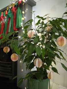 a potted plant with paper ornaments hanging from it's branches in front of a fireplace