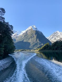 the wake of a boat traveling down a river with mountains in the background