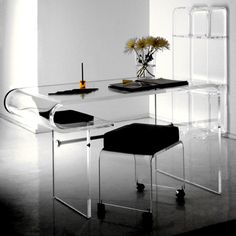 a glass table with two chairs and a vase on the top, in front of a white wall