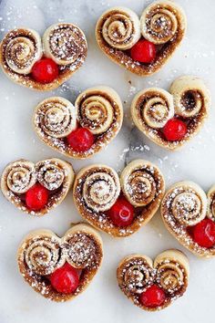 several heart shaped pastries with cherries in the middle and powdered sugar on top