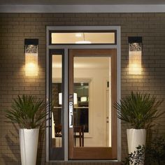 the front door to a house with potted plants on either side and lights on