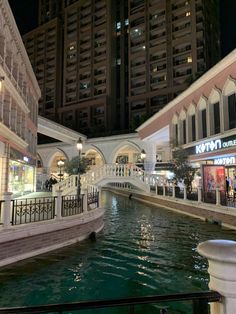 a river running through a shopping mall next to tall buildings at night with lights on