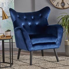 a blue chair with a pillow on it in front of a wall clock and table