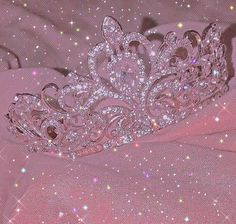 a tiara is sitting on top of a pink cloth with sparkles all around it