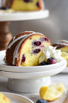 a bundt cake with white icing and blueberries is on a plate next to lemon wedges