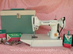 an old singer sewing machine and other items on a pink cloth covered tablecloth with a green case