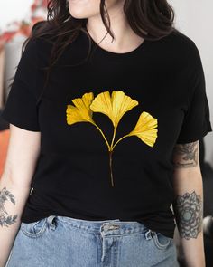 T-shirt featuring a botanical illustration of a fall Gingko leaf. Fall in love with our autumn leaves shirt you won't find anywhere else. Printed on a black cotton t-shirt, made from durable lightweight cotton. Unisex fit - boxy and long. How it's made: * All prints are original watercolor designs hand-painted by a botanical artist. * Ethically made 100% cotton t-shirts that are made to last. * T-shirts are printed and shipped by my printing partner in the US, Canada, or Europe. * By buying from this shop you are directly supporting a woman-owned small business, created out of love for plants to educate, inspire and keep us connected to the natural world. About the artist: This Shop is an extension of my botanical illustration studio, where I create hand-painted watercolor art for internat Yellow Printed T-shirt For Fall, Fall Crew Neck T-shirt With Plants Print, Black T-shirt With Floral Print For Fall, Casual T-shirt With Plants Print For Fall, Casual Plants Print T-shirt For Fall, Casual Fall T-shirt With Plant Print, Casual Fall Shirt With Plant Print, Fall Short Sleeve Shirt With Plants Print, Botanical Crew Neck T-shirt For Fall