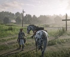 two people standing next to a horse on a lush green field in front of a cross