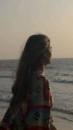 a woman standing on top of a beach next to the ocean with her hair blowing in the wind