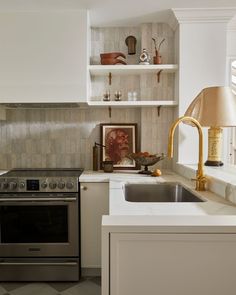 a kitchen with white cabinets and stainless steel stove top oven next to a wall mounted shelf