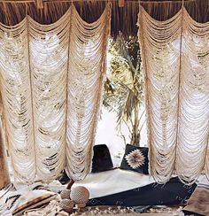 an open window with curtains and pillows on the floor in front of it, next to a potted plant