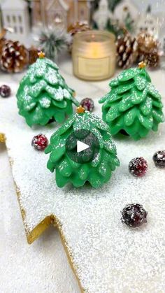 three green christmas trees sitting on top of snow covered ground next to pine cones and berries