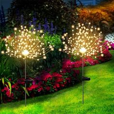 three lighted garden stakers in the grass with flowers and plants behind them at night