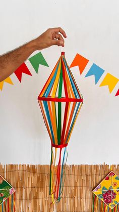 a hand holding a colorful kite in front of some paper decorations on a table top