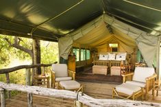 the inside of a tent with chairs and couches on wooden floor next to trees