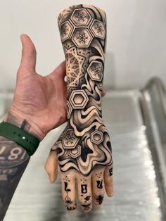 a person's hand with tattoos on it holding up their arm and the other hand