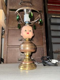 an old fashioned candle holder with a doll head on it's base and green glass beads hanging from the top