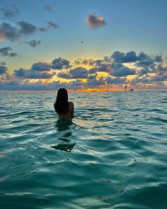 a woman is swimming in the ocean at sunset or dawn with her back turned to the camera