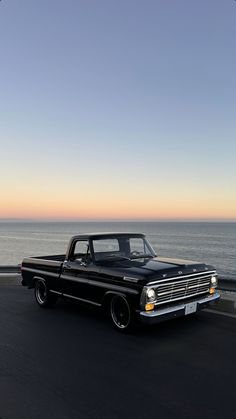 an old black truck driving down the road by the ocean