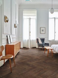 a bedroom with wood floors and white walls, including a bed in the corner between two chairs