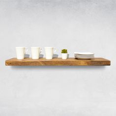 three white cups and two plates on a wooden shelf