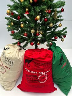 two bags are next to a small christmas tree with ornaments on it and one bag is red, the other green