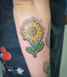 a sunflower tattoo on the arm with green leaves and a yellow flower in the center