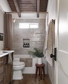 a white toilet sitting next to a bath tub in a bathroom under a wooden ceiling