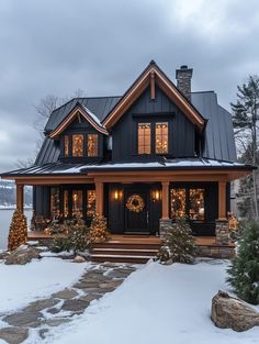 a black and brown house with christmas lights on the front door, snow covered steps leading up to it