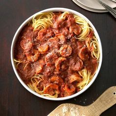 a bowl of pasta with meat and sauce on a wooden table next to utensils